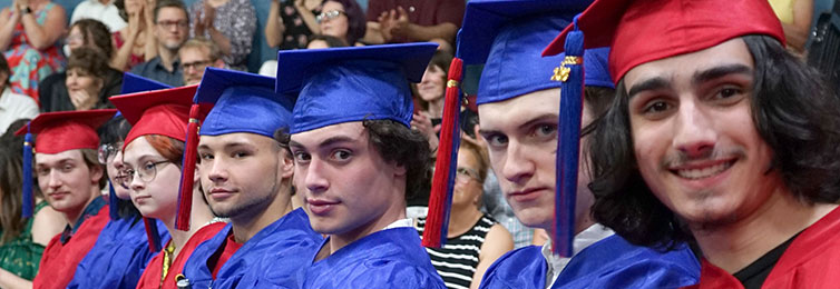 Students sitting on the bleachers with their graduation caps and gowns