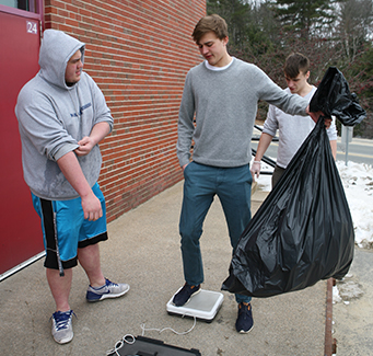 Two students outside weighing a big bag