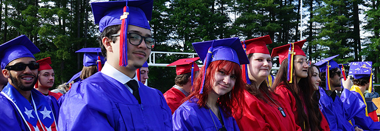 Students sitting on the bleachers with their graduation caps and gowns